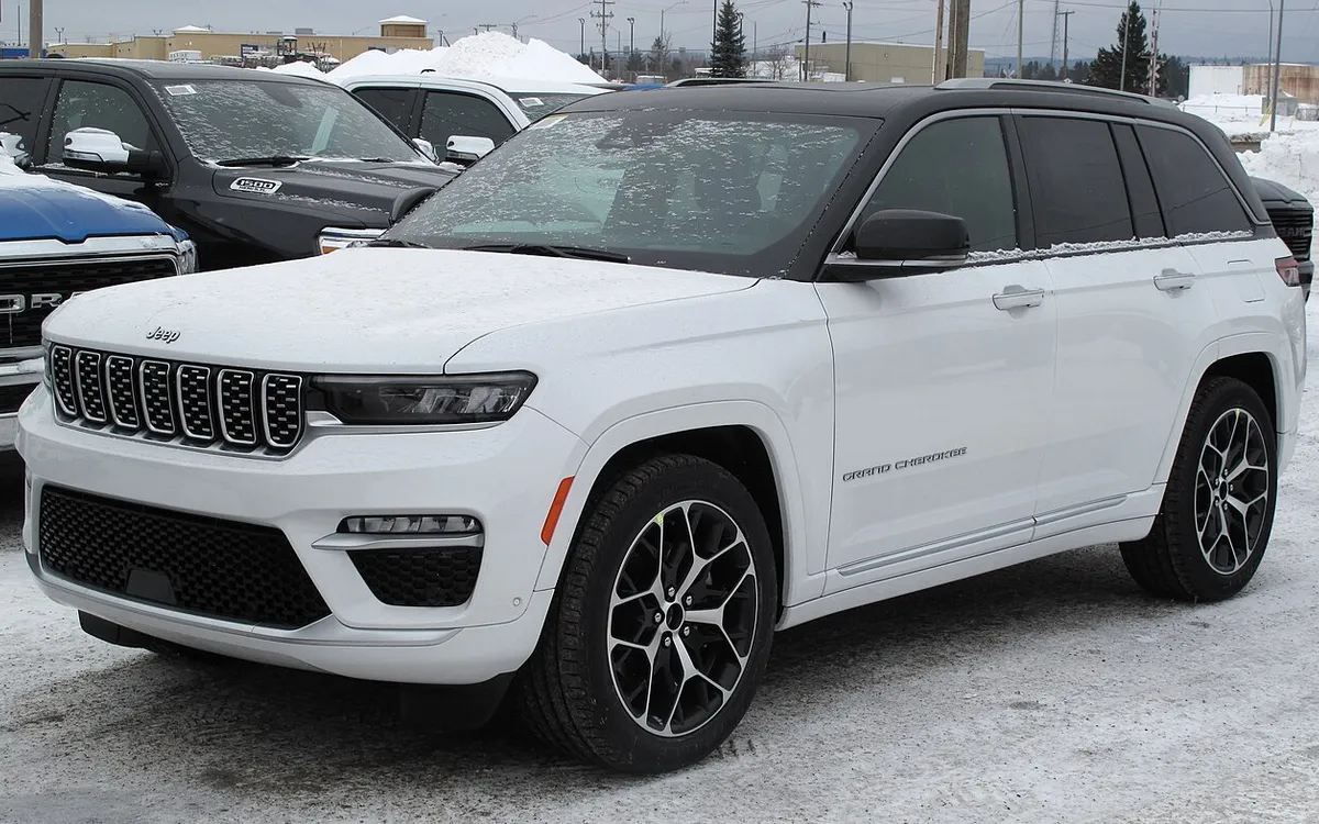 White Jeep Grand Cherokee parked in the snow next to a Ram 1500 and a Ford pickup