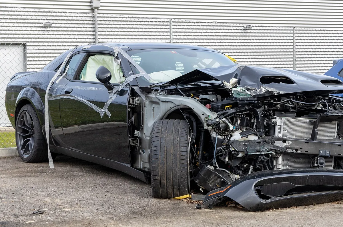 Black Dodge Challenger with a destroyed front end and deployed airbags after a crash